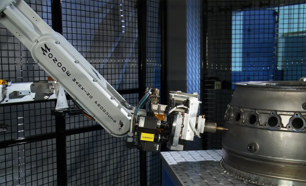 Monode robotic arm marking a metal engine component inside a safety cage