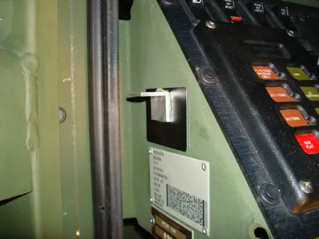 Close-up of a vehicle dashboard interior, showing a metal bracket glued next to a control panel and a specification plate with a barcode below