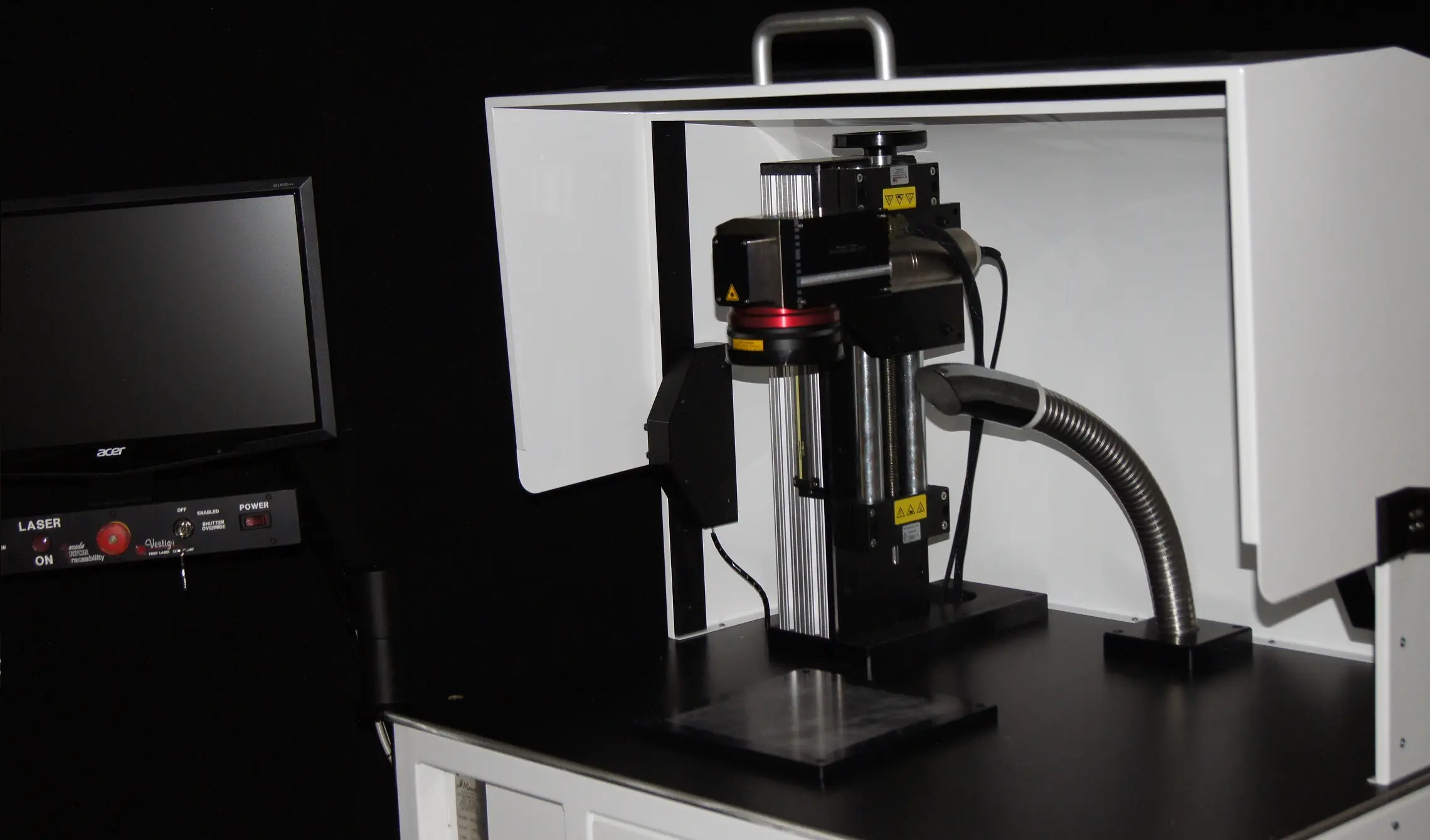 A laser marking machine set up on a workbench with an attached monitor and control panel