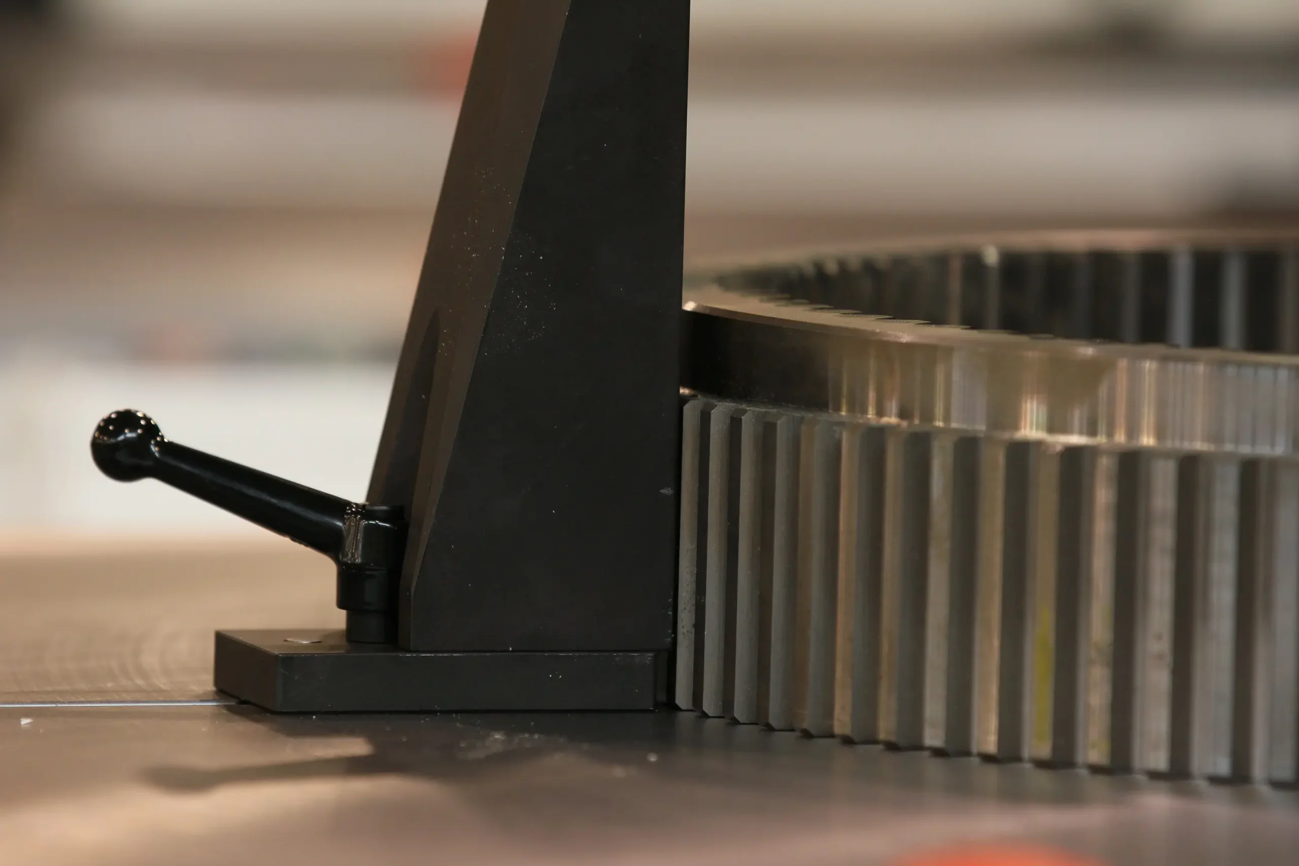 A black clamping fixture holding a large metal gear on a machine table