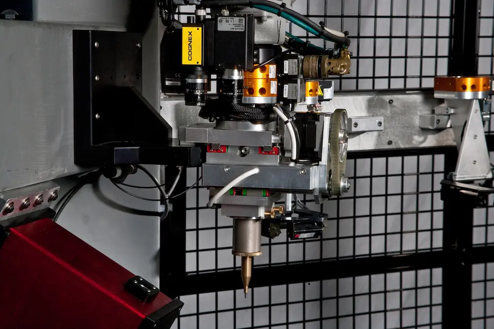 An automated industrial machine assembly with a dispensing nozzle and mounted Cognex vision system