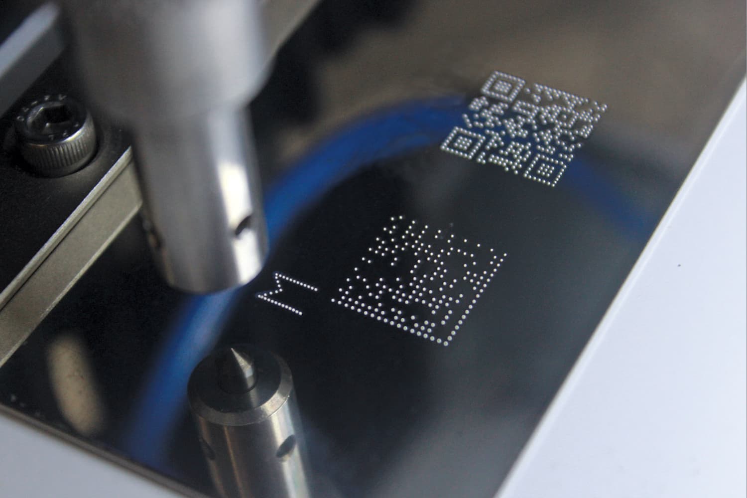 A dot peen marking machine stamping a dot-matrix QR code and letter onto a metal surface