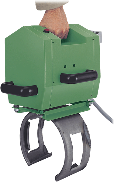A hand carrying a green, portable industrial device with a curved mounting clamp attached to the bottom