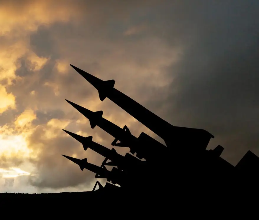 Silhouettes of four surface-to-air missiles pointed toward the sky against a cloudy sunset