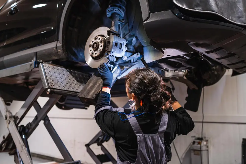 A mechanic working on the brakes of a car raised on a hydraulic lift