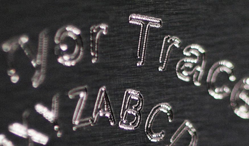 Laser-engraved text showing characters including "Traces" and "XYZABC" on a metallic surface