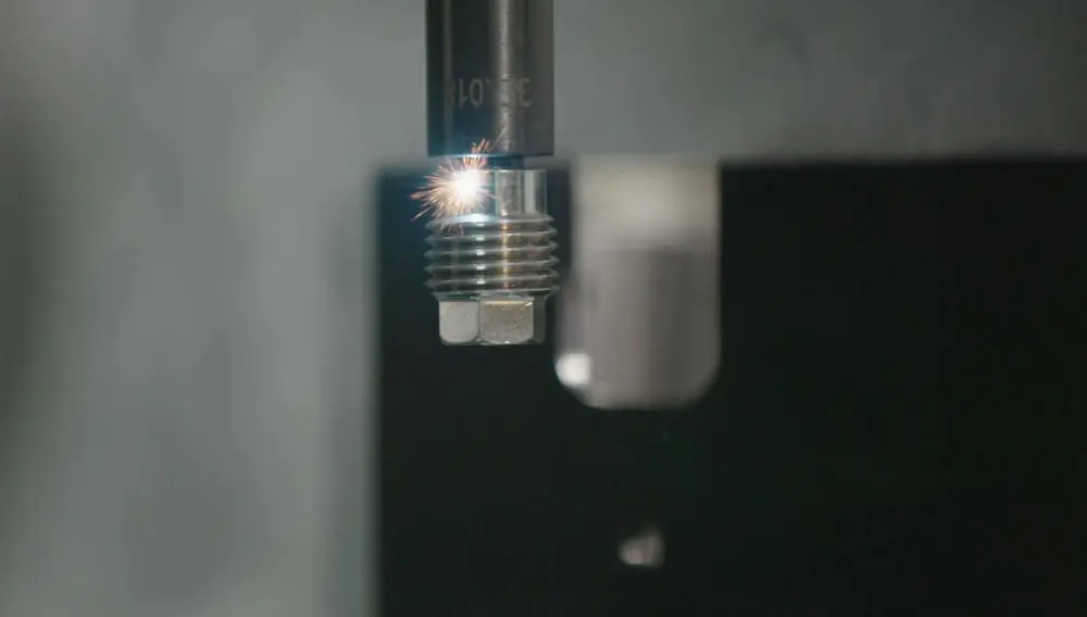 A metalworking tool cuts into a threaded metal bolt, creating a small burst of sparks